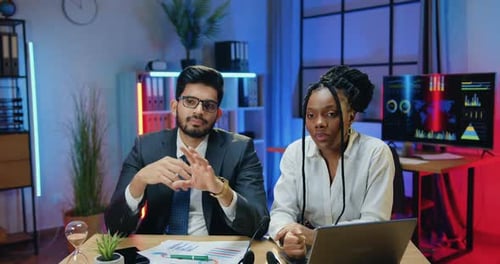 Gerentes de negocios multiétnicos sentados frente a la cámara en la oficina nocturna y grabando vídeo