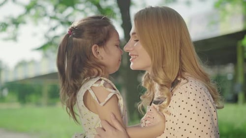 Side View Close-up of Smiling Young Blond Mother and Brunette Little Daughter Hugging and Talking in
