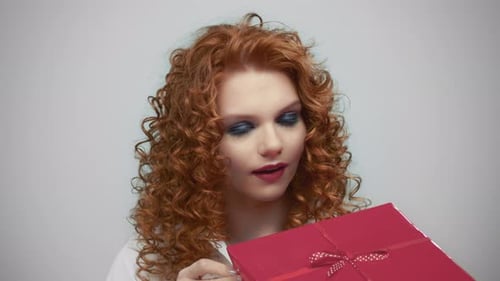 Pretty Woman Holding Gift Box in Hands. Girl Looking at Present in Studio