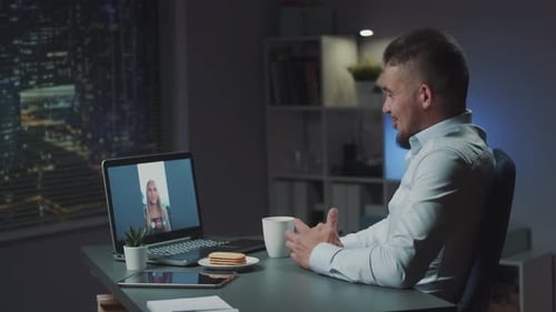 Woman Making Video Call to Her Friend From Vacations While He Working in Office in the Evening