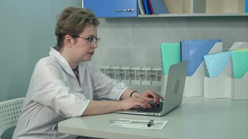 Concentrated Female Doctor in Glasses Typing on Laptop in Her Office