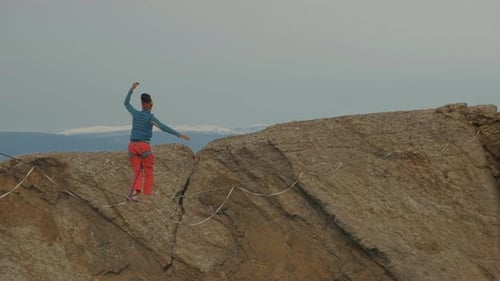 Young Adult Walking Tightrope Between Mountain Peaks