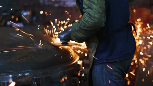 Worker Grinding Metal in Dark Factory with Sparks