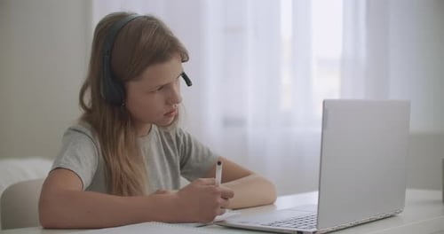 Little Girl Is Learning Online By Internet, Listening Teacher Through Headphones and Looking at