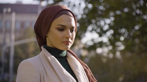 A Young Beautiful Muslim Woman Thinks About Something in a Park in an Urban Area Closeup