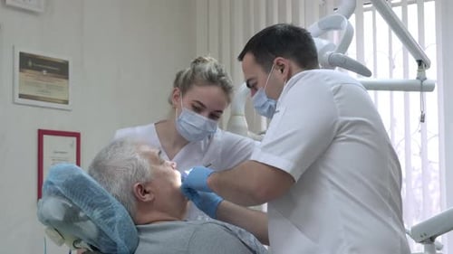 Dentist with Nurse in Protective Masks Working with Patient in Dental Clinic