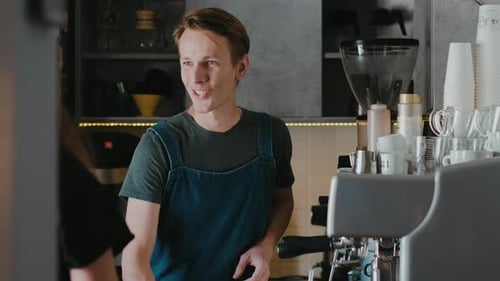 Smiling barista in a coffee shop making cappuccino coffee take away for a customer