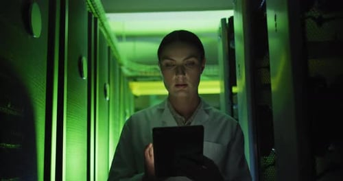 Woman Typing on Tablet in Green Lit Server Room