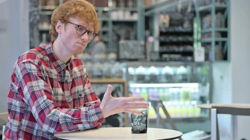 Young Man Gesturing at Table in Coffee Shop