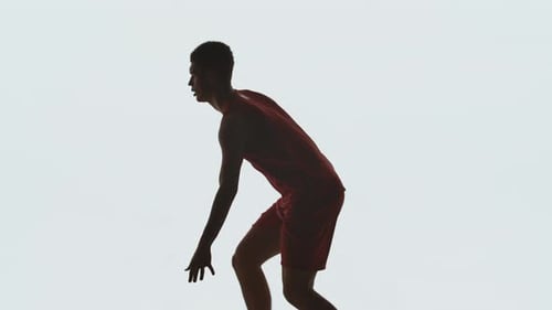 Vue latérale d'un jeune joueur de basket en uniforme de sport rouge court et dribble sur un studio blanc