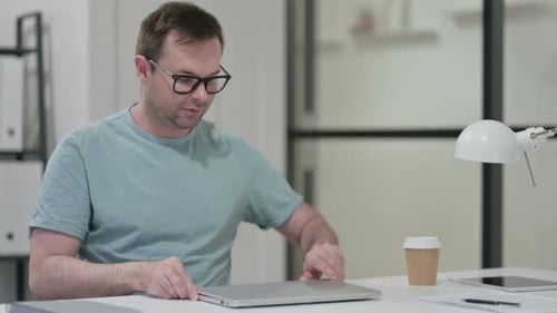 Man Opens Laptop at Desk in Modern Office