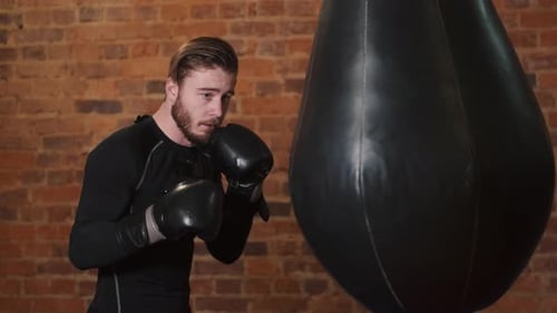 Dedicated Young Man Punching Boxing Bag at Gym