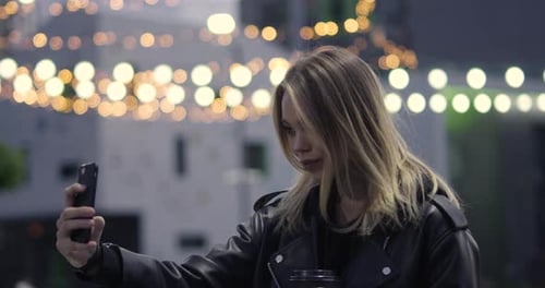 Young Girl Holds a Smartphone in Her Hand and Takes a Selfie Outside in a Modern Residential Area