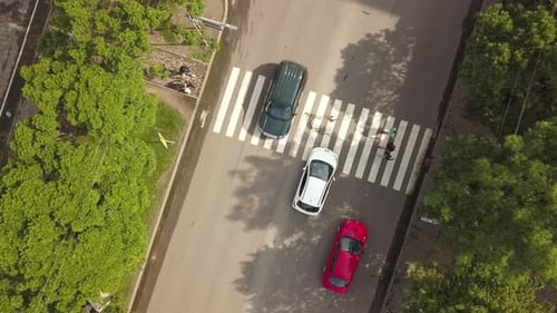 Vista aérea de cima para baixo da rua com carros em movimento e faixa de pedestres com pedestres cruzando.