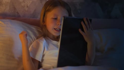 Enfant joyeux heureux de gagner dans un jeu vidéo sur tablette au lit
