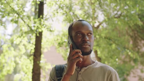 Joyeux homme afro-américain marchant dans un parc et parlant au téléphone