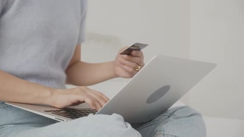 Closeup hands of woman sitting on bed using laptop computer shopping online with credit card.