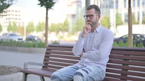 Pensive Young Adult Man Thinking While Sitting Outdoor on Bench