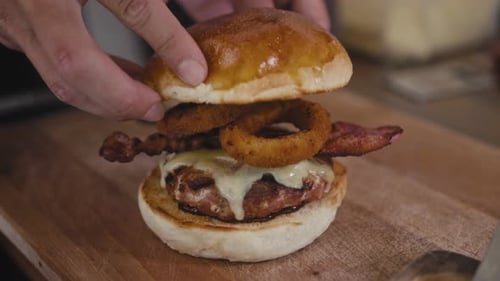 Hands Assemble Burger With Bacon and Onion Rings