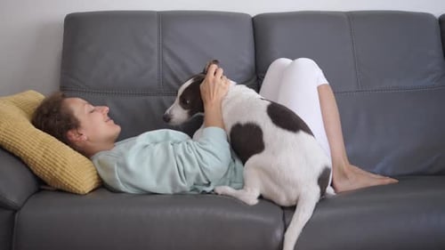 Young Happy Woman Lying With Her Dog At Home On Quarantine During Coronavirus Pandemic