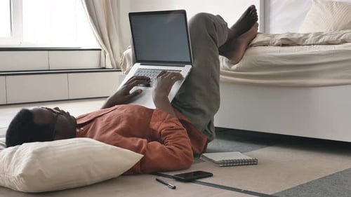 Lazy AfricanAmerican Man Works on Laptop Lying on Floor