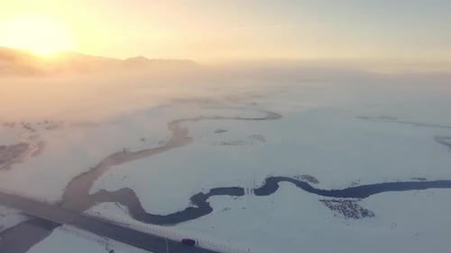Aerial view flying down toward winding river through the snow