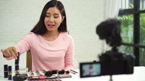 La bloguera de belleza presenta cosméticos de belleza mientras está sentada frente a la cámara para grabar un vídeo con un cepillo.