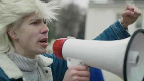 Close up caucasian woman screaming through megaphone in front and group of people manifesting in t