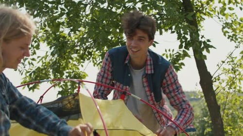 Smiling Couple Assembling Tent in Nature