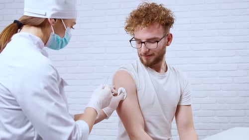 Young Man Sitting in Clinic and Nurse Giving Injection