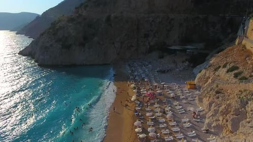 Menschen schwimmen auf hellblauem Meer am weißen Sandstrand in der Nähe des felsigen Berghangs