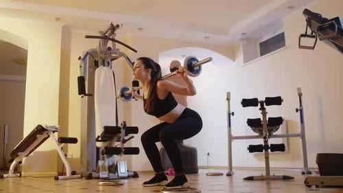 Side View Wide Shot of Slender Focused Caucasian Sportswoman Squatting with Barbell on Shoulders