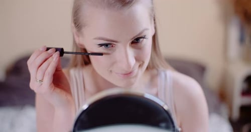 Blonde Woman Applies Mascara Looking in Mirror