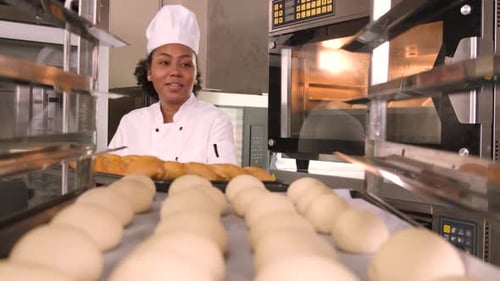 Female Baker Placing Bread in Oven in Bakery