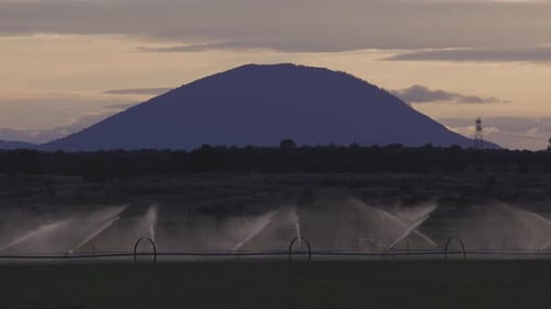 Bewässerungssprinkleranlage in einem Ackerland Spritzen von Wasser mit Berglandschaft im Hintergrund