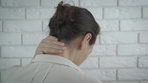 Woman Massaging Stiff Neck Against Brick Wall