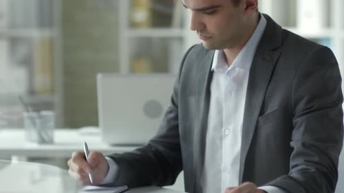 Caucasian Businessman Using Tablet and Taking Notes at Office Desk
