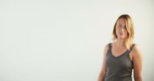 Joven mujer rubia caminando hacia la cámara y sonriendo sobre fondo blanco de estudio