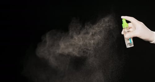 Gloved Hand Sprays Disinfectant Mist on Black