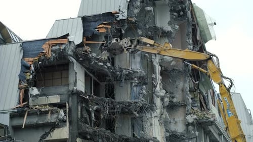 Excavator Destroys the Old Building. Demolition Work, Pieces of Concrete and Reinforcement Fall Down