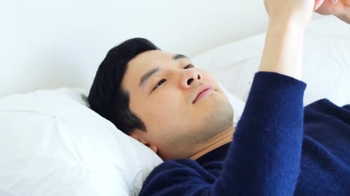 Man Lies on Bed and Uses Mobile Phone