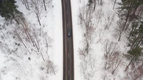 Aerial View on Car Driving Through Winter Forest Road. Scenic Winter Landscape. Top Tracking Shot.