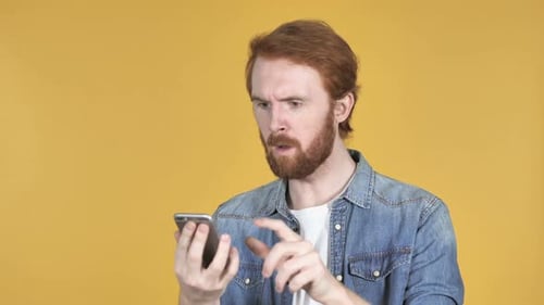 Young Man Confused by Smartphone on Yellow Background