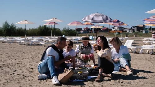Happy Family with Children and Older Generation Relaxing on the Beach and Eating Vegetables and