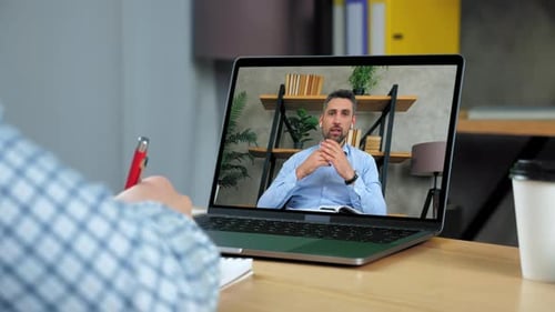 Man Employee at Home Office Writes in Notebook Listen Director Video Call Laptop
