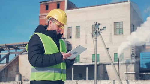 Engineer in Hard Hat Is Using a Tablet Computer in a Industry Factory