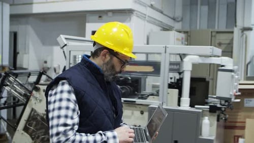 Vue latérale d'un technicien sérieux marchant avec un ordinateur portable à l'usine