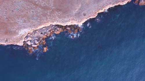 Top down aerial view of waves splash against rocky seashore, background. Flight over high cliffs of