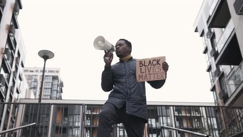 Ein junger schwarzer Mann schreit wütend mit Megaphon und hält ein Schild Black Lives Matter