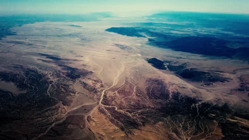 High altitude aerial flying over an arid desert landscape.